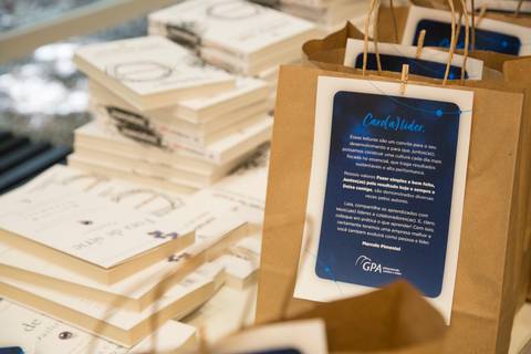 Sacola de brindes do evento Start de Ano GPA 2024, com livros e materiais corporativos dispostos ao redor, aguardando os participantes na sede do GPA em São Paulo.'