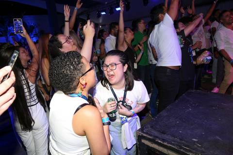 Participante do Evento de Fim de Ano GPA 2024 cantando com entusiasmo no palco, durante o show pós-palestras, animando o público na sede em São Paulo.'