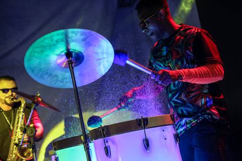 Show vibrante de tambores com purpurina sendo lançada ao ar, criando um efeito visual espetacular no palco do Evento de Fim de Ano GPA 2024 na sede em São Paulo.'