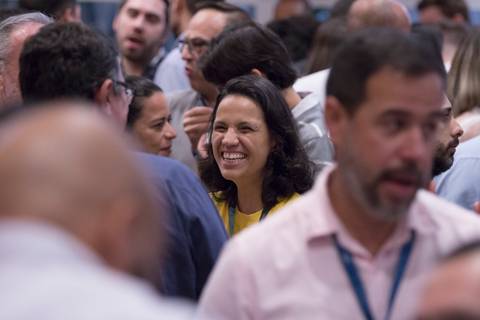 Participante do Evento de Fim de Ano GPA 2024 sorrindo e interagindo no coffee break, aproveitando o momento de descontração na sede em São Paulo.'