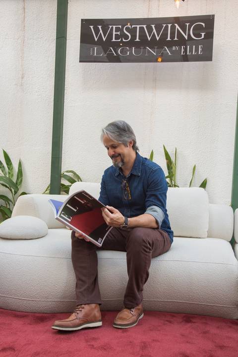 Participante do evento Westwing + ELLE no Restaurante Chou em São Paulo, tranquilamente sentado no sofá modular da Westwing, folheando uma revista ELLE com interesse.'