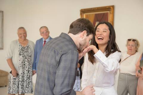 Noivo beijando delicadamente a mão da noiva, que sorri radiantemente, em um gesto romântico durante a cerimônia de casamento no 13º Cartório do Butantã, em São Paulo.'