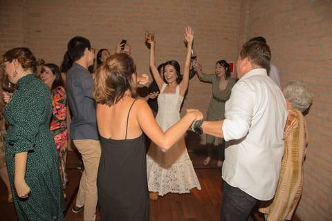 Noiva de braços erguidos, celebrando com euforia no centro de uma ciranda de convidados, em um momento de pura alegria e união na festa de casamento no Restaurante Cantaloup em São Paulo.'