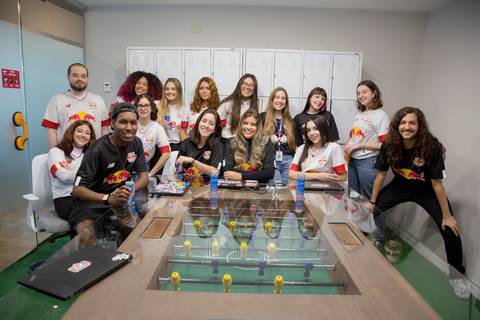 Fotografia criativa de um grupo de estagiários da Red Bull Brasil 2024 posando juntos como um time de futebol, demonstrando espírito de equipe na sede da empresa em São Paulo.'