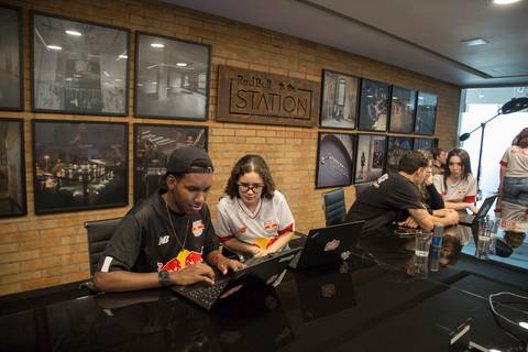 Fotografia dos dois estagiários trabalhando em conjunto em uma mesa com um notebook, sorrindo e focados, imagem utilizada no banner do programa de estágio Red Bull Brasil 2024, registrada na sede da Red Bull em São Paulo.'