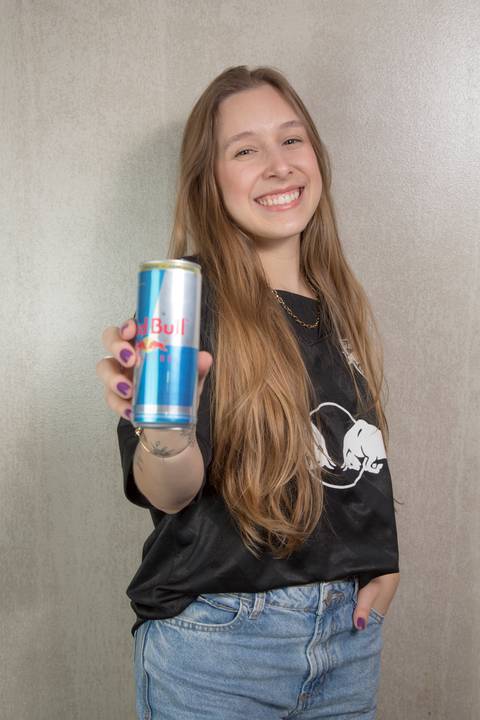 Retrato de uma jovem estagiária sorridente segurando uma lata gelada de Red Bull, com o logotipo da marca em destaque, na sede da Red Bull Brasil em São Paulo.'