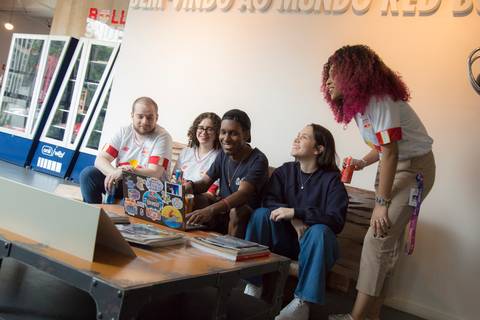Fotografia do grupo de estagiários sentados relaxadamente em um sofá e sorrindo enquanto olham para um notebook, imagem utilizada no banner do programa de estágio Red Bull Brasil 2024, tirada na sede da Red Bull em São Paulo.