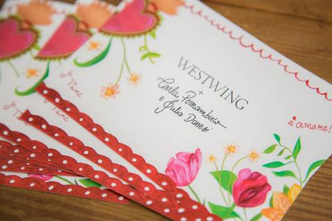 Convites do evento de lançamento da coleção Westwing com Carla Pernambuco e Julia Danesi, dispostos sobre uma mesa, evidenciando a parceria e o design do material gráfico no Restaurante Carlota em São Paulo.'