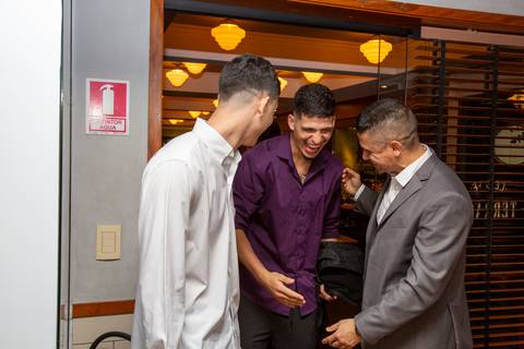 O marido cumprimentando convidados com uma gargalhada contagiante, em um momento de pura alegria e descontração na festa de casamento no Restaurante Le Bife em São Paulo.'