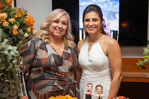 Outra imagem da esposa posando com uma convidada, com uma postura diferente, mas mantendo o sorriso e a interação amigável na festa no Restaurante Le Bife em São Paulo.'