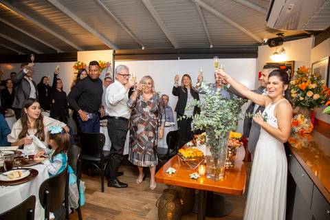 O casal recém-casado fazendo um brinde com taças, com todos os convidados visíveis ao fundo, celebrando a união em grande estilo no Restaurante Le Bife em São Paulo.'