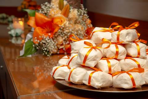 Doce bem-casado cuidadosamente embalado em destaque, com o buquê da noiva levemente desfocado ao fundo, simbolizando a tradição e o romance do casamento no Restaurante Le Bife em São Paulo.'