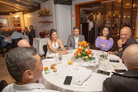 O casal recém-casado sentado em uma mesa de convidados, conversando animadamente e desfrutando da companhia de amigos e familiares no Restaurante Le Bife em São Paulo.'
