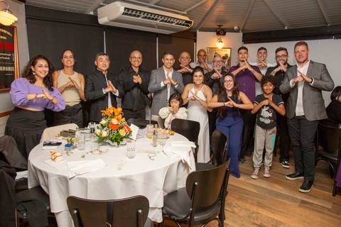 Casal recém-casado posando com convidados da escola de kung fu, todos fazendo a pose de Kinrai, em um momento único e divertido na festa no Restaurante Le Bife em São Paulo.'