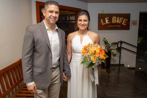 Casal recém-casado posando em frente ao Restaurante Le Bife em São Paulo, a noiva segurando seu buquê, em um registro elegante do dia do casamento.'