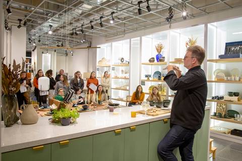Chef Carlos Bertolazzi em primeiro plano, com os participantes do workshop e o ambiente da loja Westwing de Moema ao fundo, durante o evento culinário em São Paulo.'