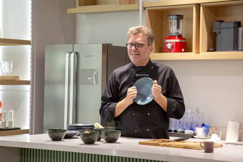 Chef Carlos Bertolazzi explicando a importância da apresentação do prato, utilizando uma peça da Porto Brasil, durante o evento na loja Westwing de Moema, São Paulo.'