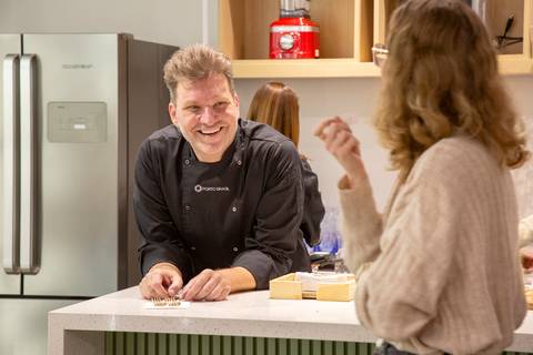 Chef Carlos Bertolazzi em uma conversa espontânea e sorridente com uma participante do workshop, interagindo de forma descontraída na loja Westwing de Moema, São Paulo.'