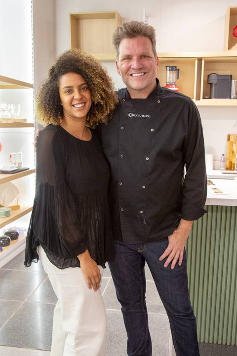 Chef Carlos Bertolazzi em outra foto posada com uma convidada, com um gesto amigável, durante o evento culinário na loja Westwing de Moema, São Paulo.'