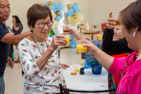A aniversariante japonesa de 80 anos brindando com seus convidados, com um sorriso de felicidade, em um momento de união na festa em Boituva-SP.'