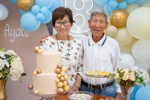 A aniversariante japonesa de 80 anos e seu marido juntos na mesa do bolo, em um registro carinhoso de parceria e celebração em Boituva-SP.'
