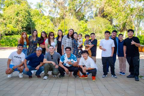 Grupo de primos jovens posando de forma descontraída para uma foto na área externa verde da festa de 80 anos em Boituva-SP.'