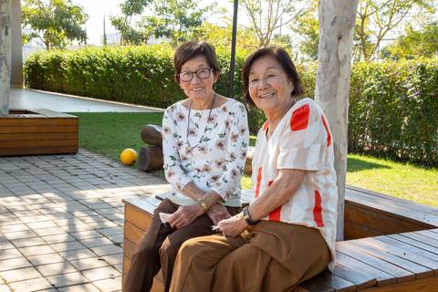 A aniversariante japonesa de 80 anos em uma conversa amigável com uma convidada na área externa da festa em Boituva-SP, desfrutando do ambiente natural.'
