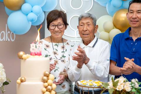 A aniversariante japonesa de 80 anos cantando 'Parabéns a Você' com alegria e emoção, acompanhada pelos convidados em sua festa em Boituva-SP.'