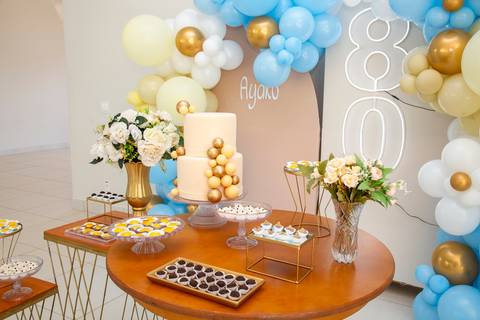 Mesa do bolo festiva para o aniversário de 80 anos em Boituva-SP, adornada com doces, arranjos florais, o nome da aniversariante e o número 80 em destaque ao fundo'