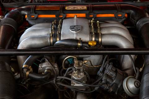 Detalhe do motor de um carro Porsche, mostrando a complexidade de suas peças e componentes, em manutenção na oficina DAN911 em São Paulo.'