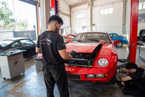 Mecânico da oficina DAN911 abrindo o capô de um Porsche em São Paulo, preparando-se para inspeção ou manutenção do motor do veículo esportivo.'