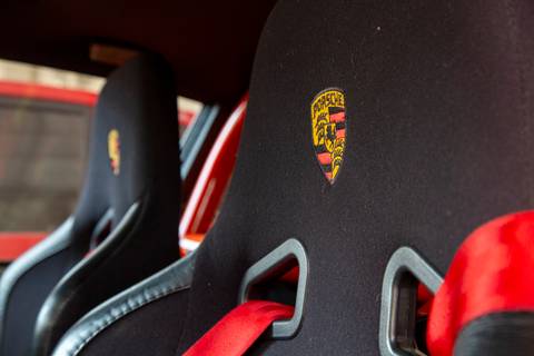 Close-up do encosto do banco do motorista de um Porsche, exibindo o escudo da marca costurado ou gravado, detalhando o interior de luxo na oficina DAN911.'