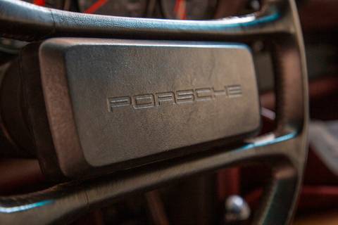 Close-up do volante de um carro Porsche, com o logotipo da marca em destaque, revelando a atenção aos detalhes e o design interno dos veículos na oficina DAN911.'