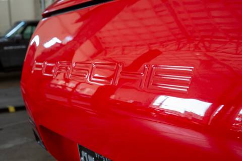 Detalhe em close-up do nome 'Porsche' elegantemente gravado no para-choque traseiro de um carro, destacando o acabamento do veículo na oficina DAN911 em São Paulo.'