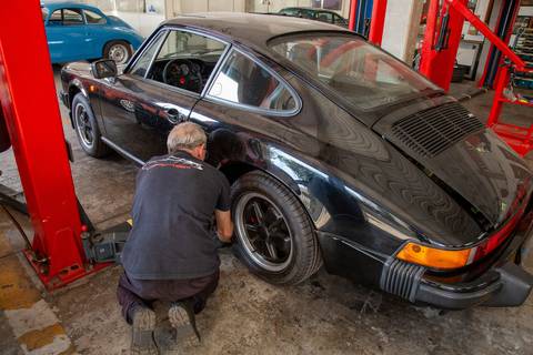 Mecânico da oficina DAN911 em São Paulo concentrado, realizando ajustes finos ou inspeção em um veículo Porsche, demonstrando perícia e atenção.'