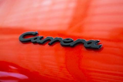 Detalhe da inscrição 'Carrera' no exterior de um veículo Porsche, em plano fechado, realçando o nome icônico da linha esportiva na oficina DAN911 em São Paulo.'
