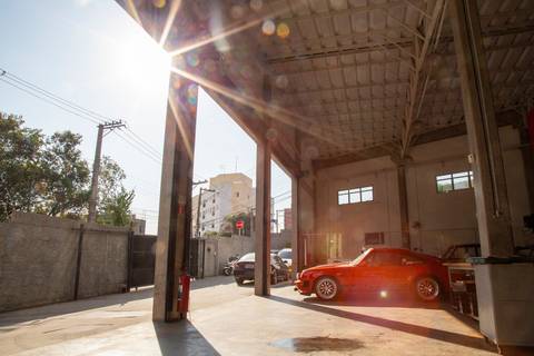 Raios de sol entrando e iluminando o interior da oficina DAN911 em São Paulo, destacando o ambiente de trabalho e os veículos Porsche.'