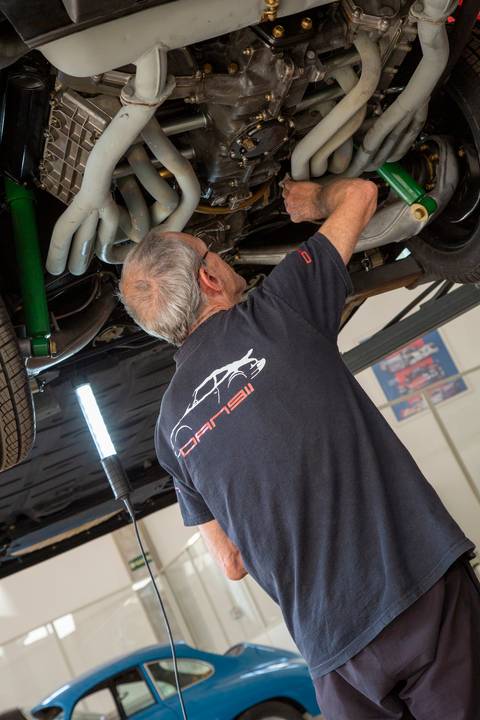 Plano fechado no rosto e parte superior do corpo do mecânico da oficina DAN911 em São Paulo, capturando sua expressão de concentração e expertise enquanto trabalha em um Porsche.'