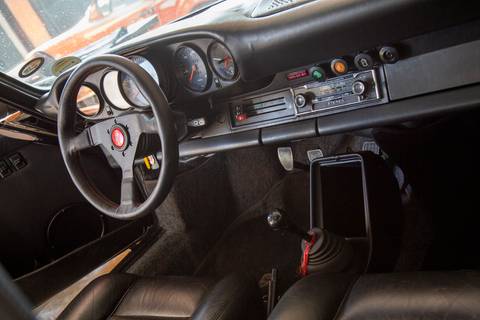 Vista interna detalhada de um Porsche, focando no painel de instrumentos, volante e rádio, revelando o design clássico do cockpit na oficina DAN911 em São Paulo.'
