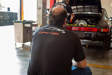 Mecânico da oficina DAN911 em São Paulo, cuidadosamente observando e avaliando um carro Porsche, transmitindo expertise e dedicação.'