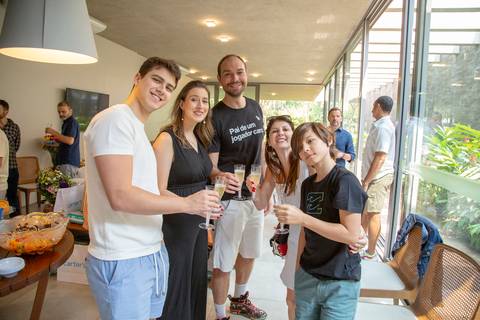 O casal anfitrião do chá de bebê em São Paulo fazendo um brinde com taças, acompanhado por convidados, em celebração à vida do futuro bebê.'