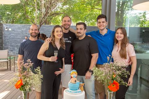O casal anfitrião posando junto com um grupo de amigos na mesa do bolo do chá de bebê em São Paulo, registrando a alegria e o apoio dos mais chegados.'