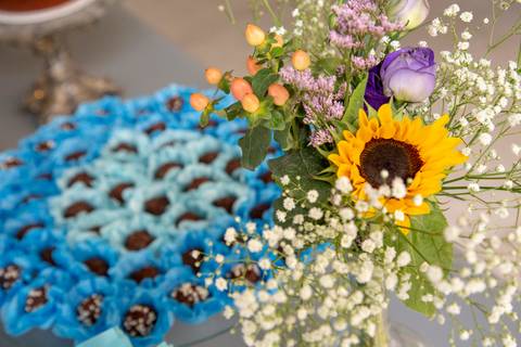 Delicado arranjo de flores frescas em primeiro plano, com doces personalizados desfocados no segundo plano, criando uma composição charmosa na decoração do chá de bebê em São Paulo.'