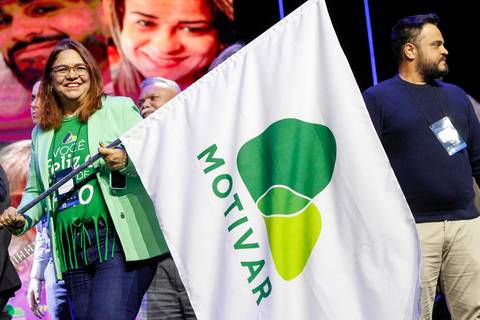 Participante do Evento GPA no Espaço Unimed em São Paulo, caminhando com uma bandeira branca onde se lê a palavra 'Motivar', inspirando a plateia presente.'