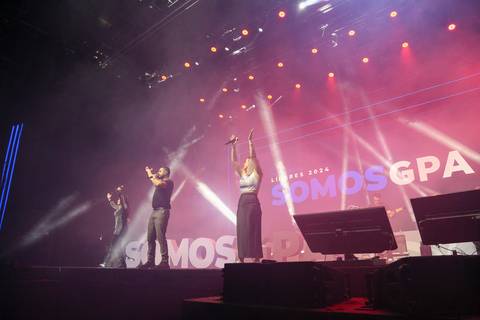 Três cantores da banda do show pós-evento do GPA, no palco do Espaço Unimed em São Paulo, entoando a música com carisma e interagindo com a plateia.'