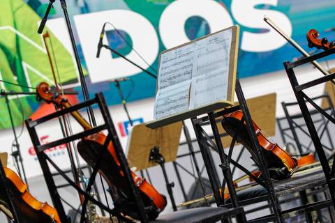 Detalhamento de instrumentos musicais clássicos, como violinos e violoncelos, posicionados no palco do Evento GPA no Espaço Unimed em São Paulo, indicando a performance orquestral.'