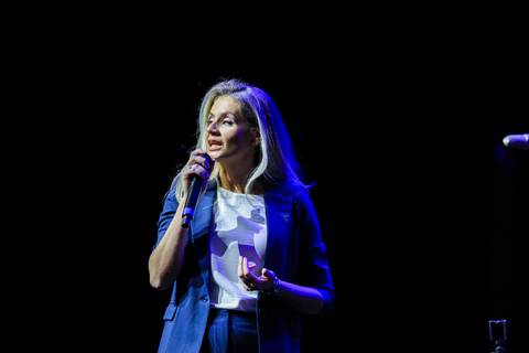 Apresentadora carismática no palco do Evento GPA no Espaço Unimed em São Paulo, sorrindo e interagindo com o público de mais de mil pessoas.'