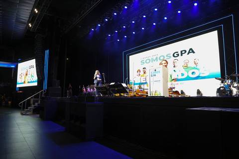 Plano aberto da apresentadora no palco principal do Evento GPA no Espaço Unimed em São Paulo, com o vasto público de mais de mil pessoas ao fundo, no início da cerimônia.'
