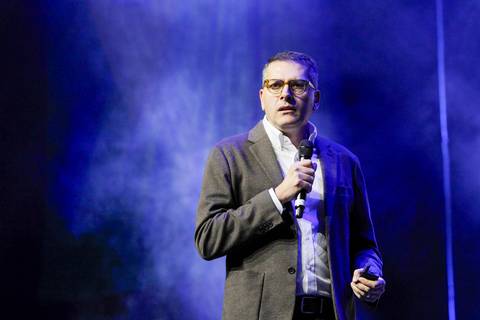 O SEO do GPA falando com paixão e gesticulando no palco do Espaço Unimed em São Paulo, transmitindo uma mensagem inspiradora para o público massivo do evento.'