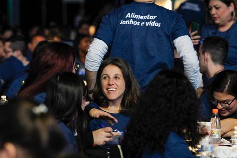 Mulher no público do Evento GPA no Espaço Unimed em São Paulo, sorrindo abertamente e engajada com as apresentações no palco.'